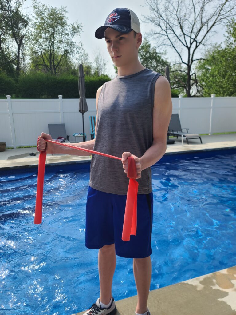 Il nuotatore competitivo, Alex Ailatis, che dimostra un esercizio di allungamento della banda di terapia per correggere la spalla del nuotatore.